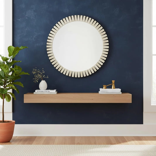 Round mirror with decorative frame on a blue wall above a wooden shelf with decor items.