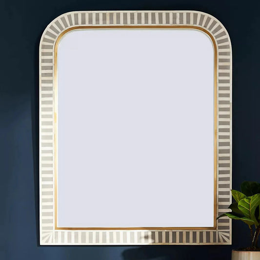 A rectangular mirror with hand-inlaid bone in a stripe pattern with gray resin, mounted on a wall above a wooden cabinet with a brass strip for a luxurious look.