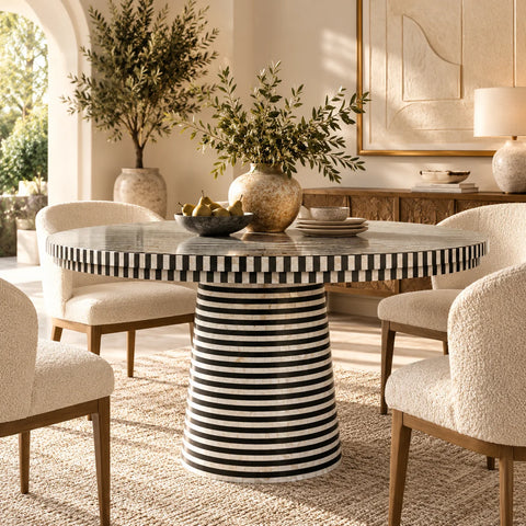 A mothet of pearl inlay round dining table with a black-and-white striped pedestal base surrounded by cream upholstered dining chairs in a warm, sunlit dining room.
