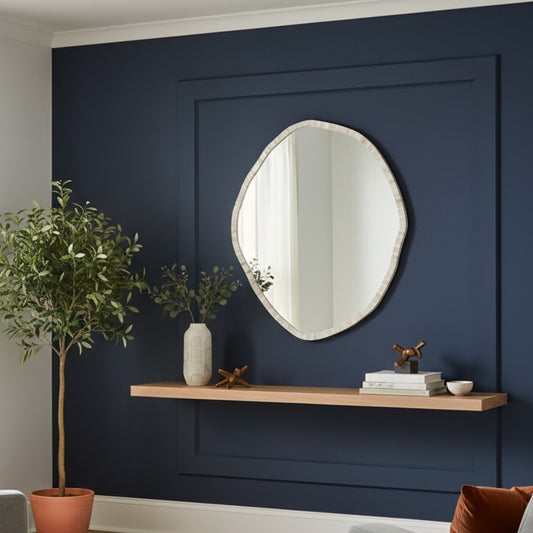 Round mirror on a navy wall with a wooden shelf below containing decorative items.