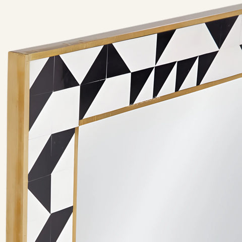Decorative mirror with geometric black and white pattern and gold frame on a white background