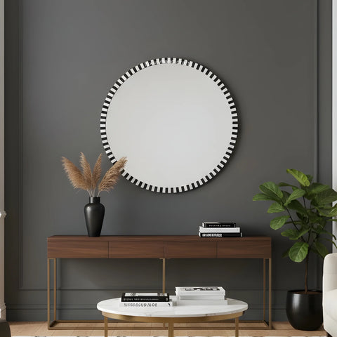 Round mirror with black and white striped frame above a wooden console table in a room.