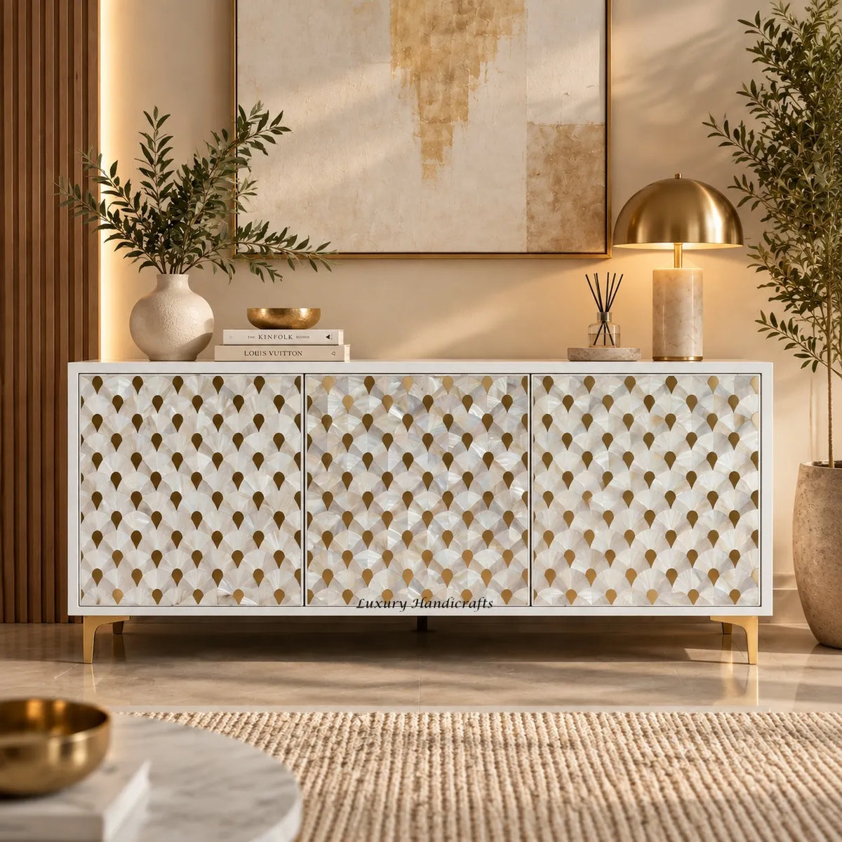 A modern white mother of pearl inlay buffet with gold geometric leaf-patterned doors, styled in a warm, contemporary living room setting with a gold dome lamp, books, and plants.