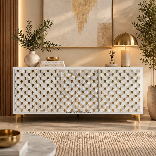 A modern white mother of pearl inlay buffet with gold geometric leaf-patterned doors, styled in a warm, contemporary living room setting with a gold dome lamp, books, and plants.